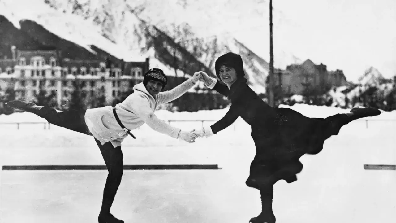 Dwie kobiety w strojach z epoki tańczą na lodzie, tworząc piękny obraz łyżwiarstwa figurowego. Ich pozy i uśmiechy świadczą o radości z tej zimowej dyscypliny, kt&oacute;ra ma bogatą historię.