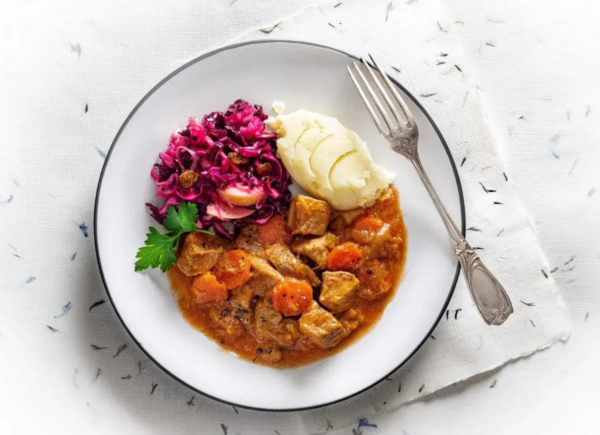 Gulasz z kawałkami mięsa i marchewki, podany z purée ziemniaczanym i czerwoną kapustą. Idealny pomysł, czy marynować mięso na gulasz.