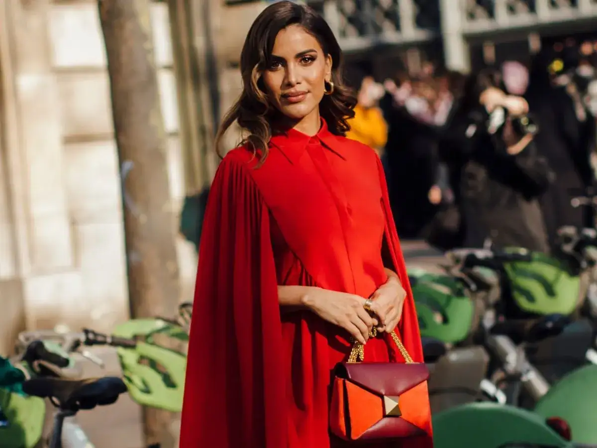 Elegancka kobieta w czerwonej sukni z peleryną, z torebką w dłoni. Idealny przykład, jaki makijaż do czerwonej sukienki.