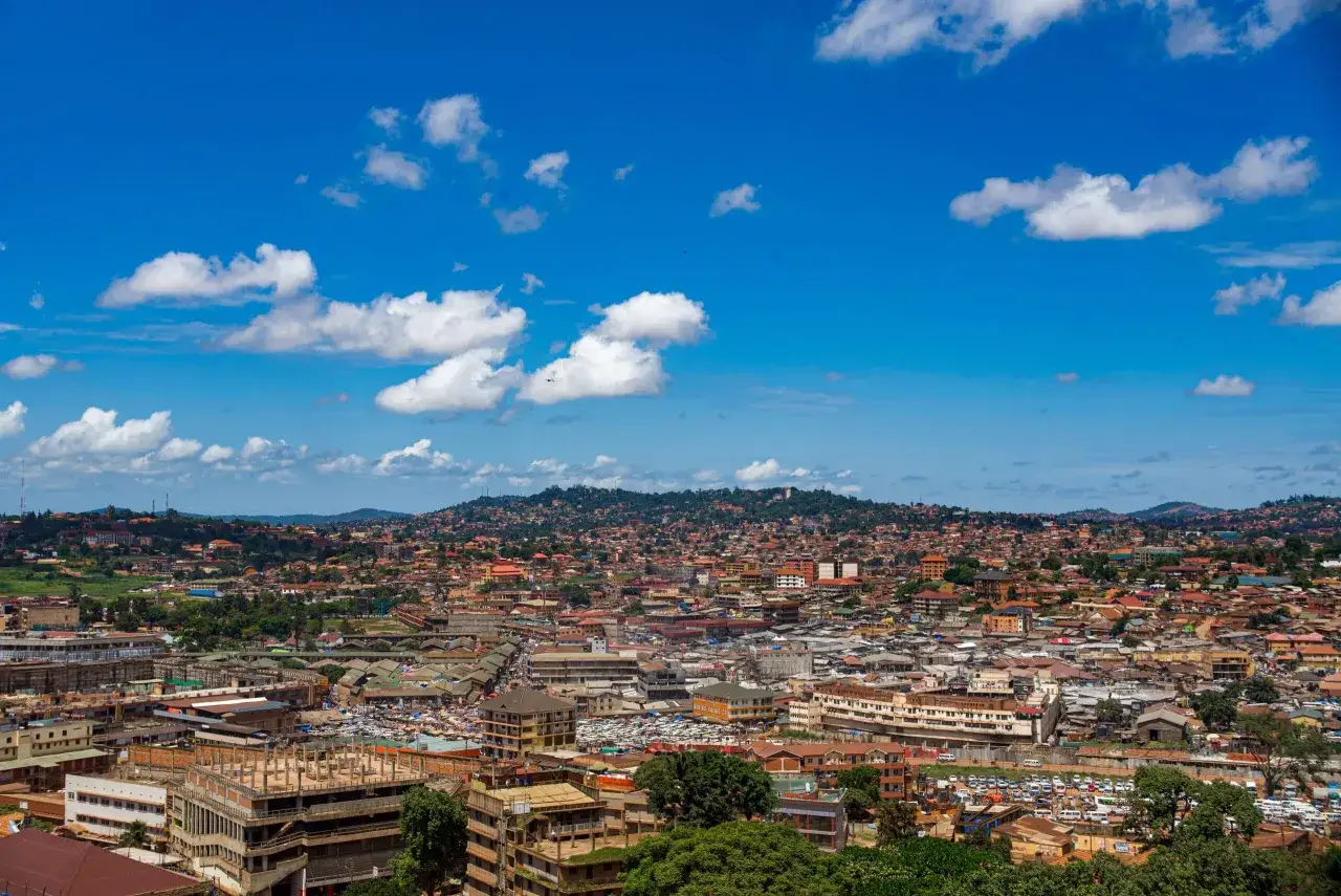 Rozległy krajobraz miejski stolicy Ugandy, Kampali, z gęsto zabudowanymi wzg&oacute;rzami i błękitnym niebem z białymi chmurami.