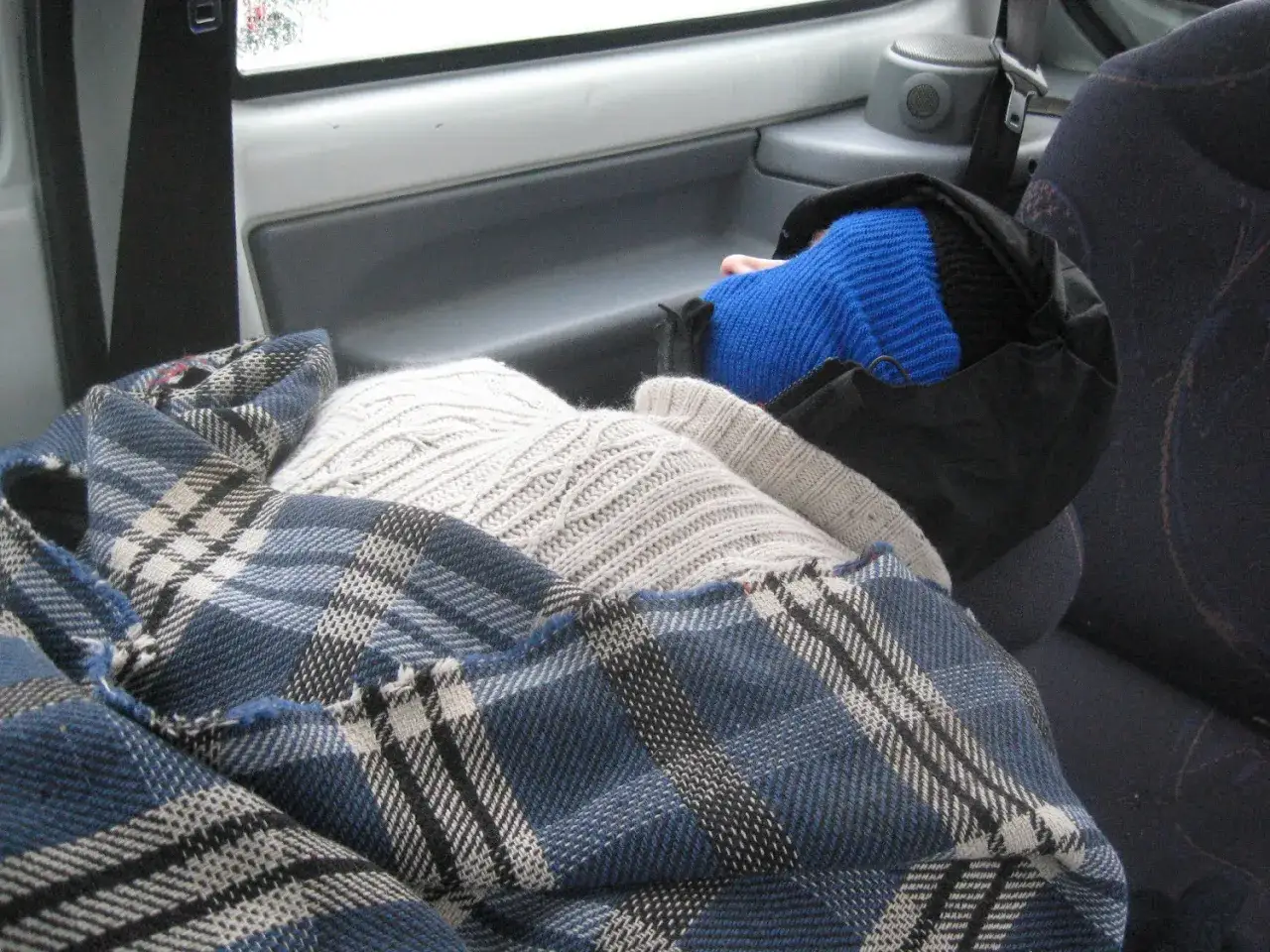 Osoba śpi w samochodzie, otulona kocami. To typowe dla podr&oacute;ży i spania w samochodzie w Europie.