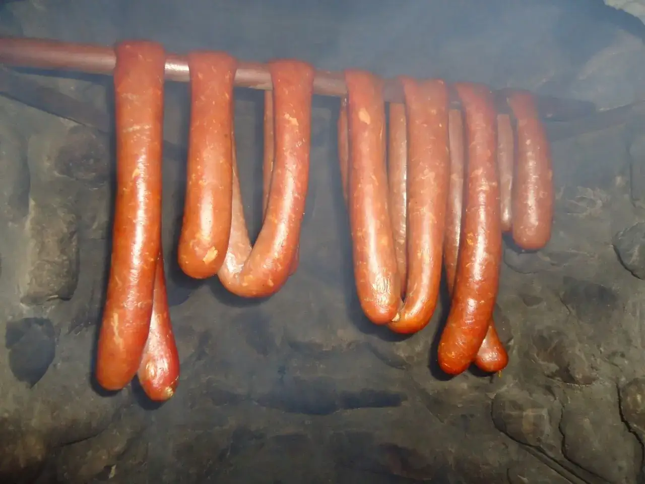 Wędzenie kiełbasy bez parzenia: wiszące, rumiane kiełbaski w dymie.