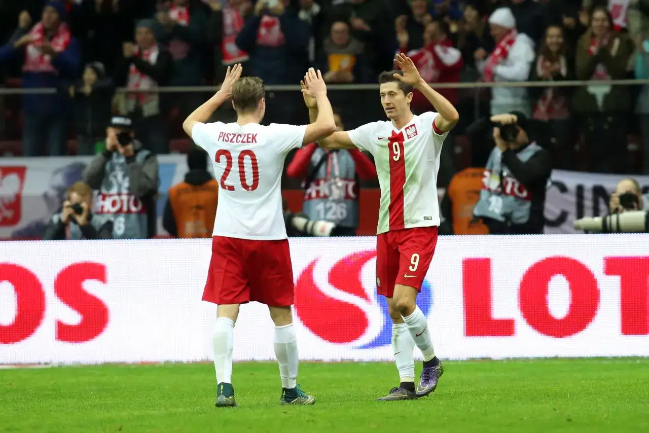 Dw&oacute;ch piłkarzy w biało-czerwonych strojach, jeden z numerem 20, drugi z numerem 9, świętuje na boisku.