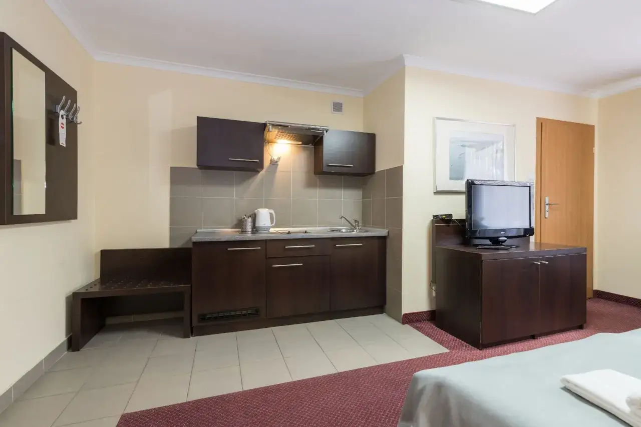 Pokój w resort spa plaza z aneksem kuchennym, lustrem, ławką i telewizorem.