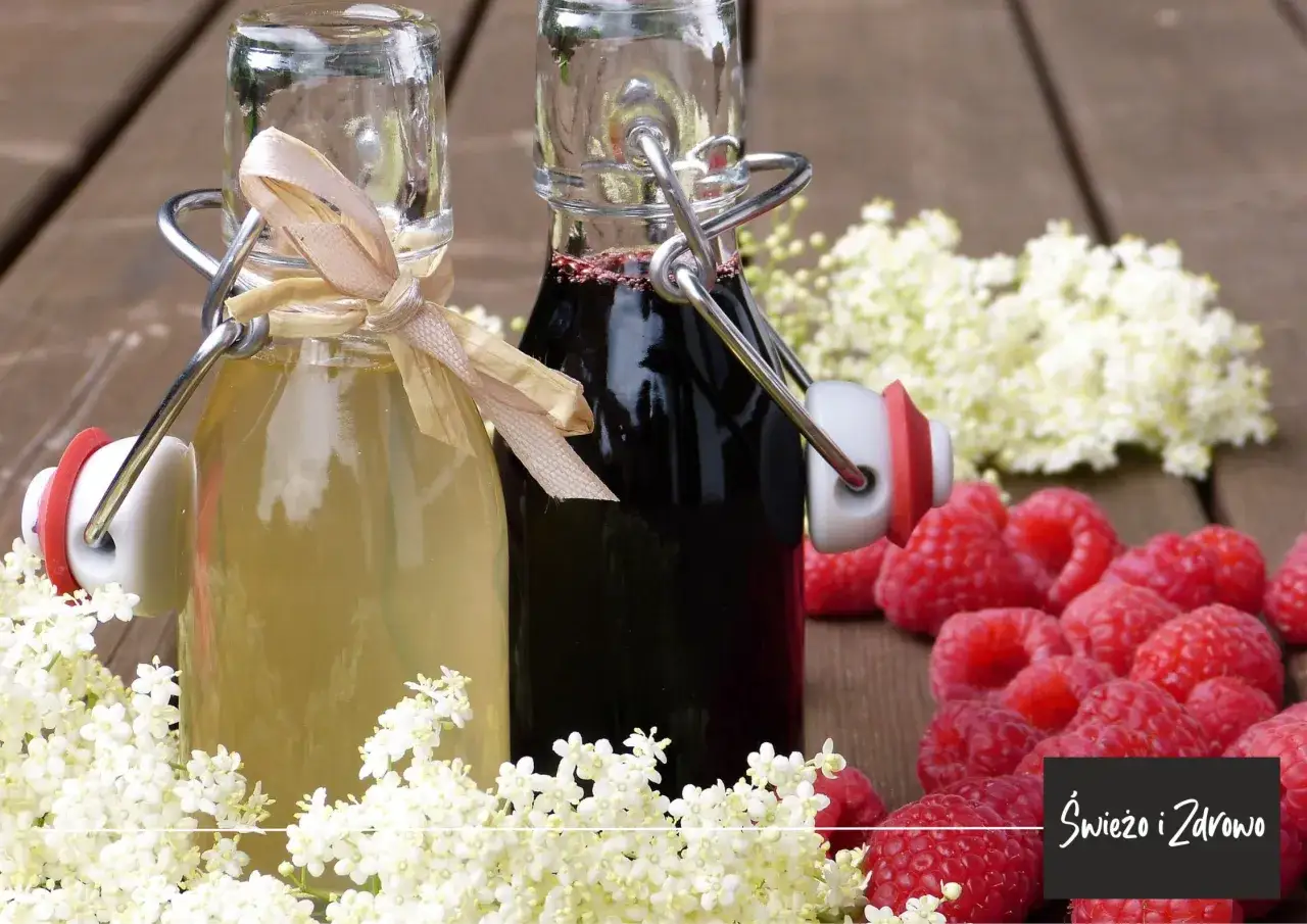 Dwa syropy z czarnego bzu: jasny i ciemny, otoczone kwiatami czarnego bzu i malinami. Syrop z czarnego bzu na co? Na odporność i zdrowie!