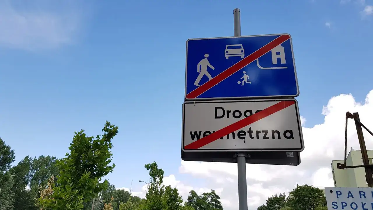 Znaki drogowe informują o końcu drogi wewnętrznej. Widać na nich symbol samochodu, pieszego i dziecka grającego w piłkę, przekreślone czerwonym pasem.
