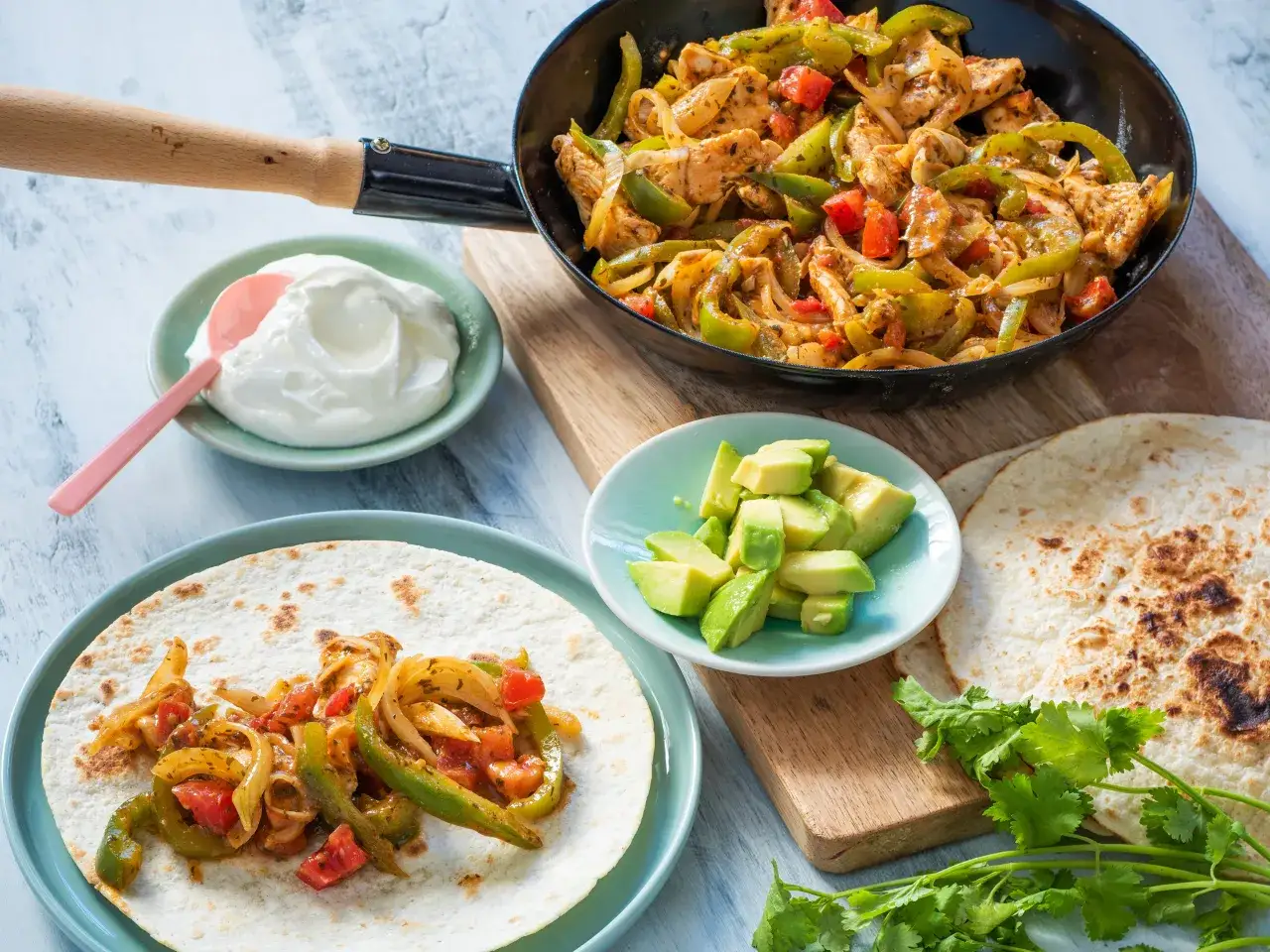 Fajitas co to? Aromatyczne kurczak z papryką i cebulą na tortilli, podane z awokado i śmietaną.