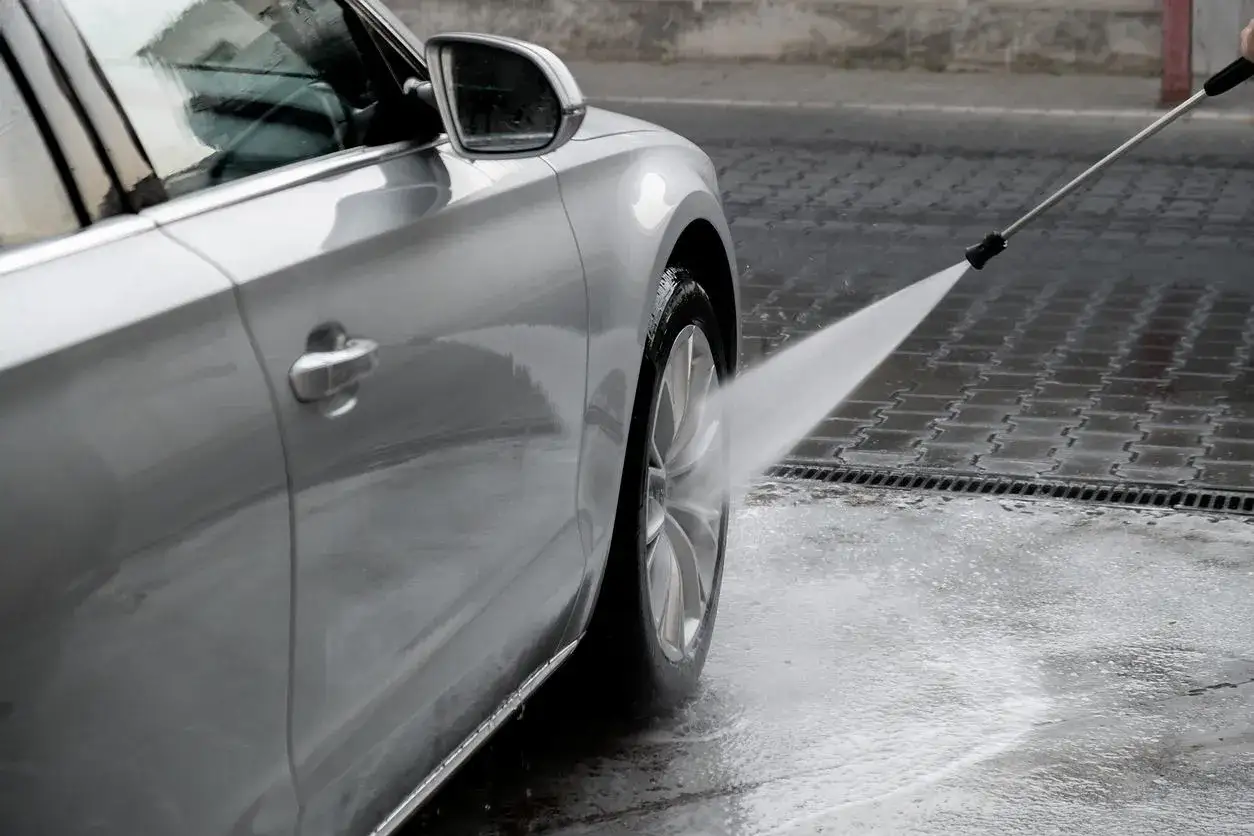 Srebrne auto na myjni, strumień wody z myjki ciśnieniowej spływa po karoserii. Pokazujemy, jak myć auto na myjni.