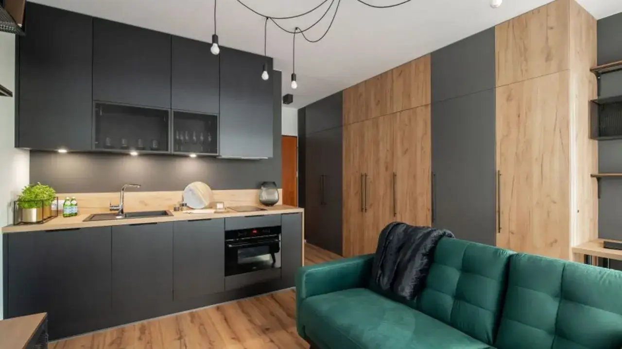 Nowoczesna aranżacja mieszkania 50m2 w bloku: ciemna kuchnia, drewniane fronty szaf i zielona kanapa tworzą stylową całość.