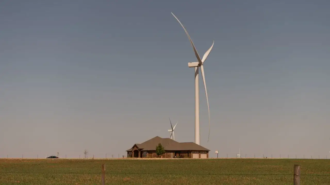 Dom z garażem i drzewem na tle ogromnych wiatrak&oacute;w. Czy wiatraki są szkodliwe? To pytanie zadaje sobie wielu, patrząc na te potężne konstrukcje.