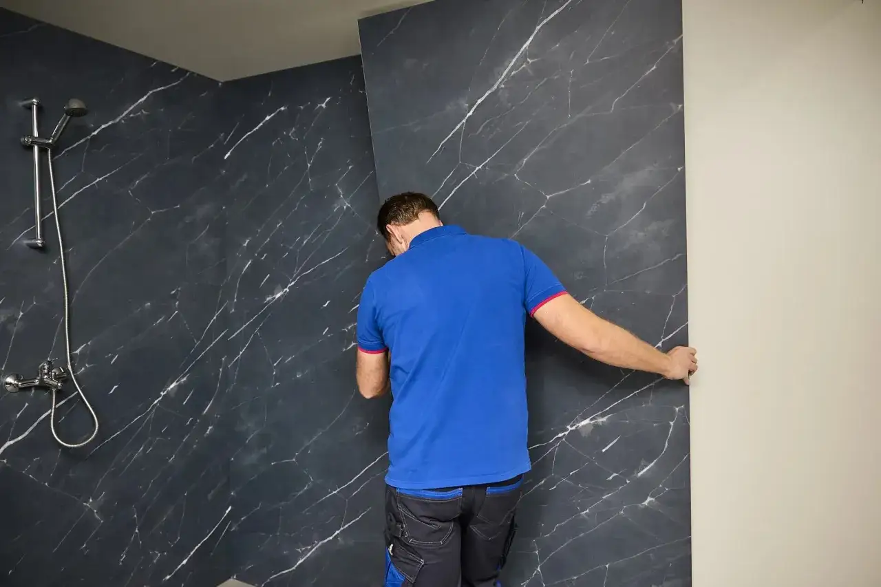 Montaż paneli ściennych PCV w łazience. Pracownik dopasowuje ciemny panel imitujący marmur.