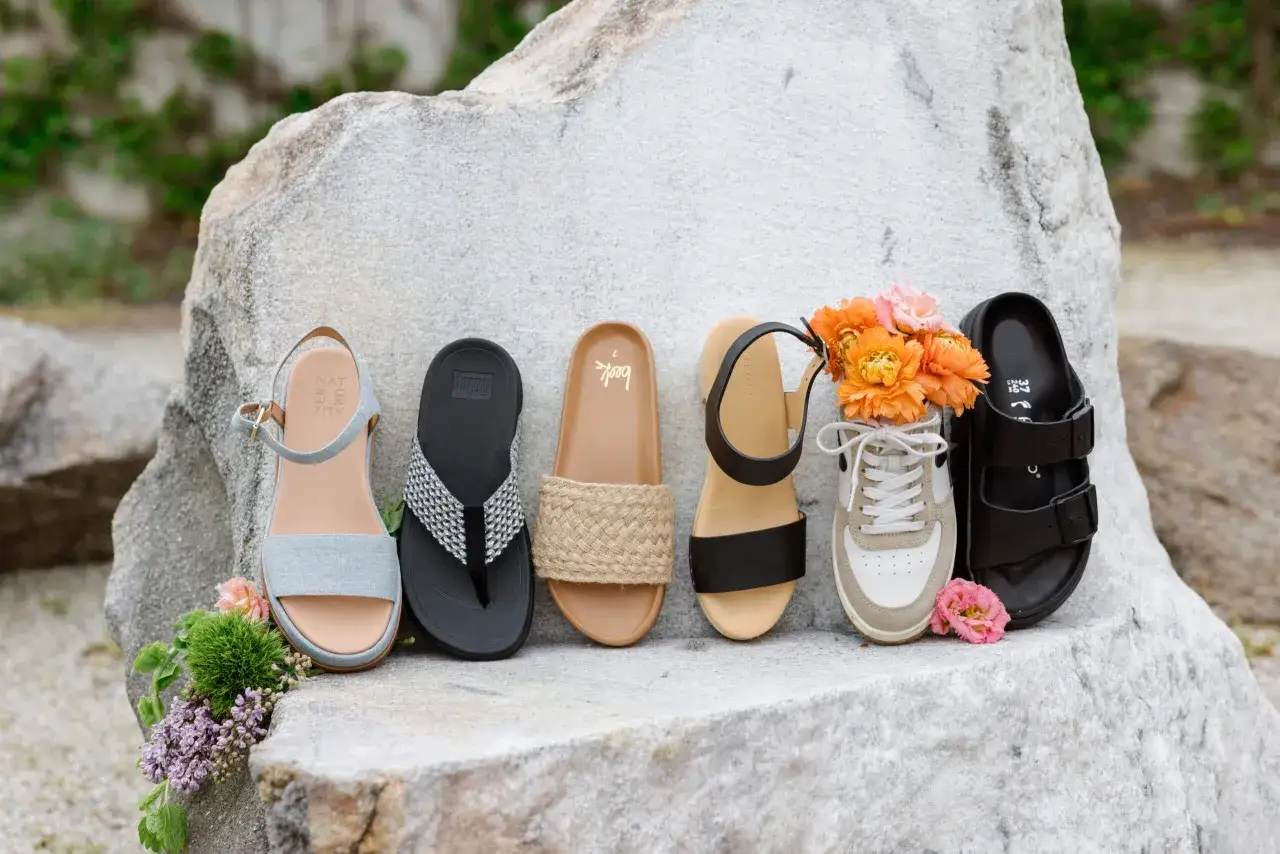 Letnie buty bez skarpet: szare sandałki, czarne klapki, plecione espadryle, czarne sandałki, sneakersy z kwiatami i czarne klapki.
