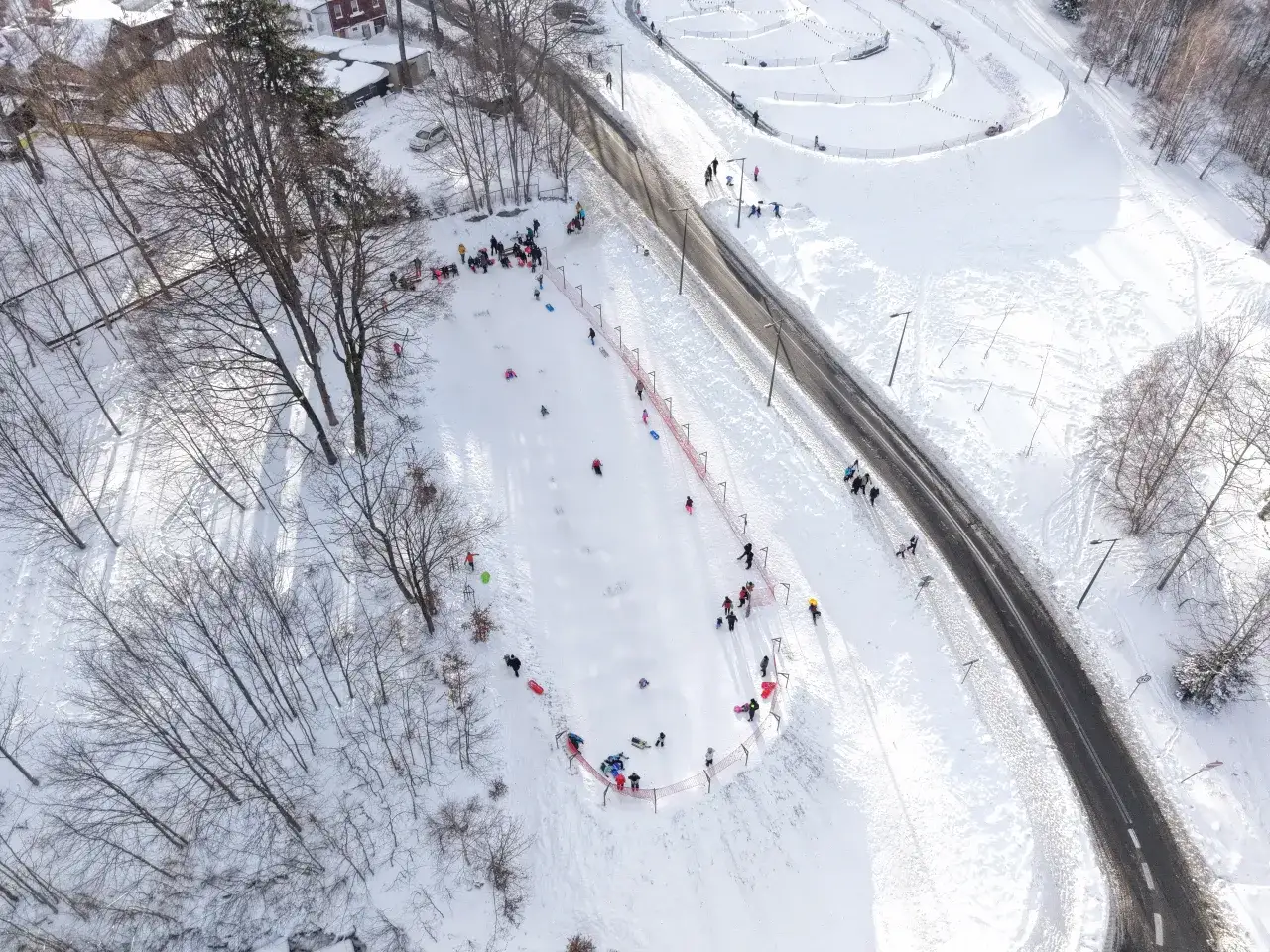 Dzieci i dorośli cieszą się zimowym torem saneczkowym, zjeżdżając na sankach po ośnieżonym stoku.