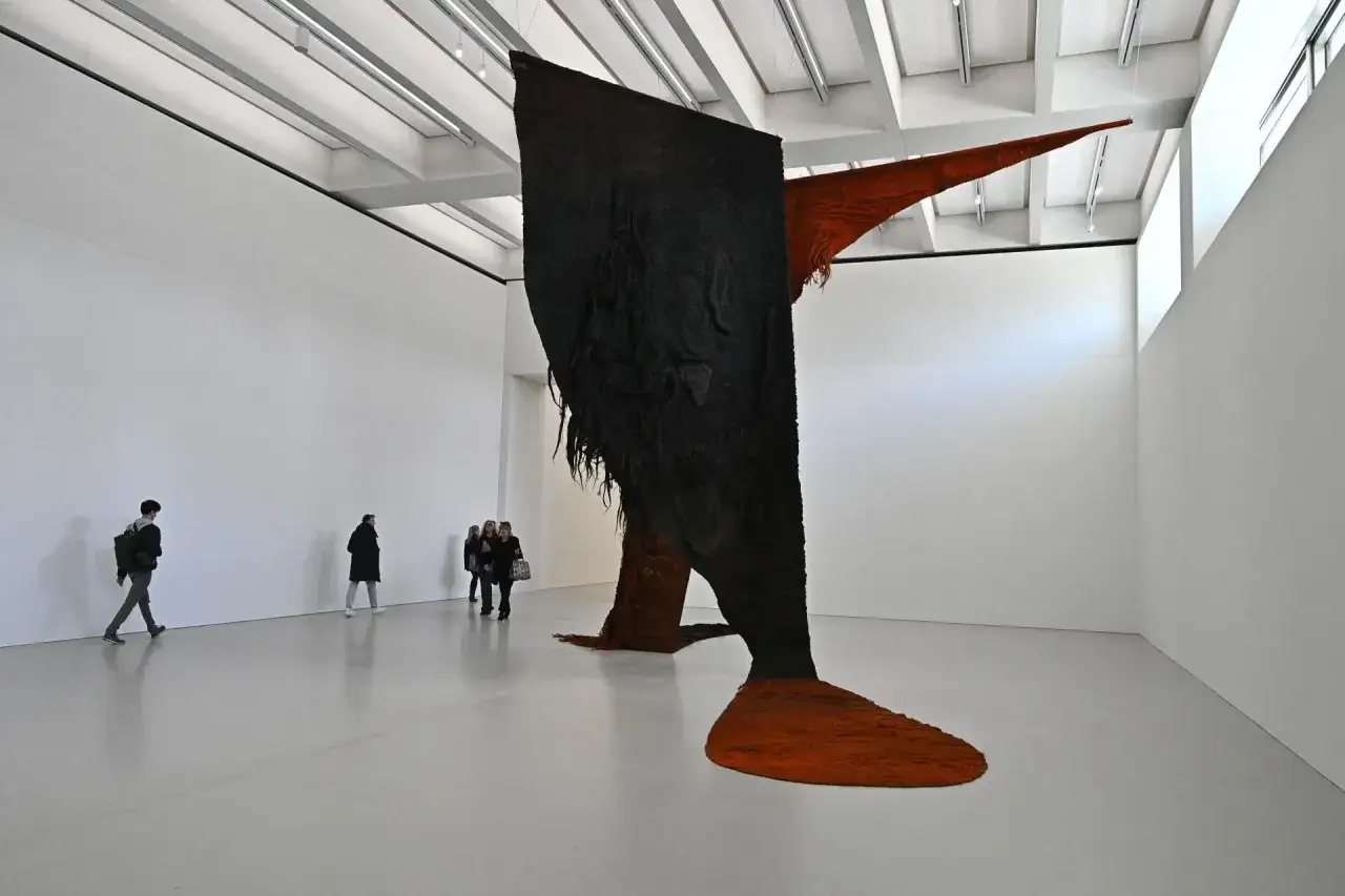 Wystawa w muzeum sztuki nowoczesnej: masywna, wisząca instalacja z czarnego i pomarańczowego materiału przyciąga uwagę zwiedzających.