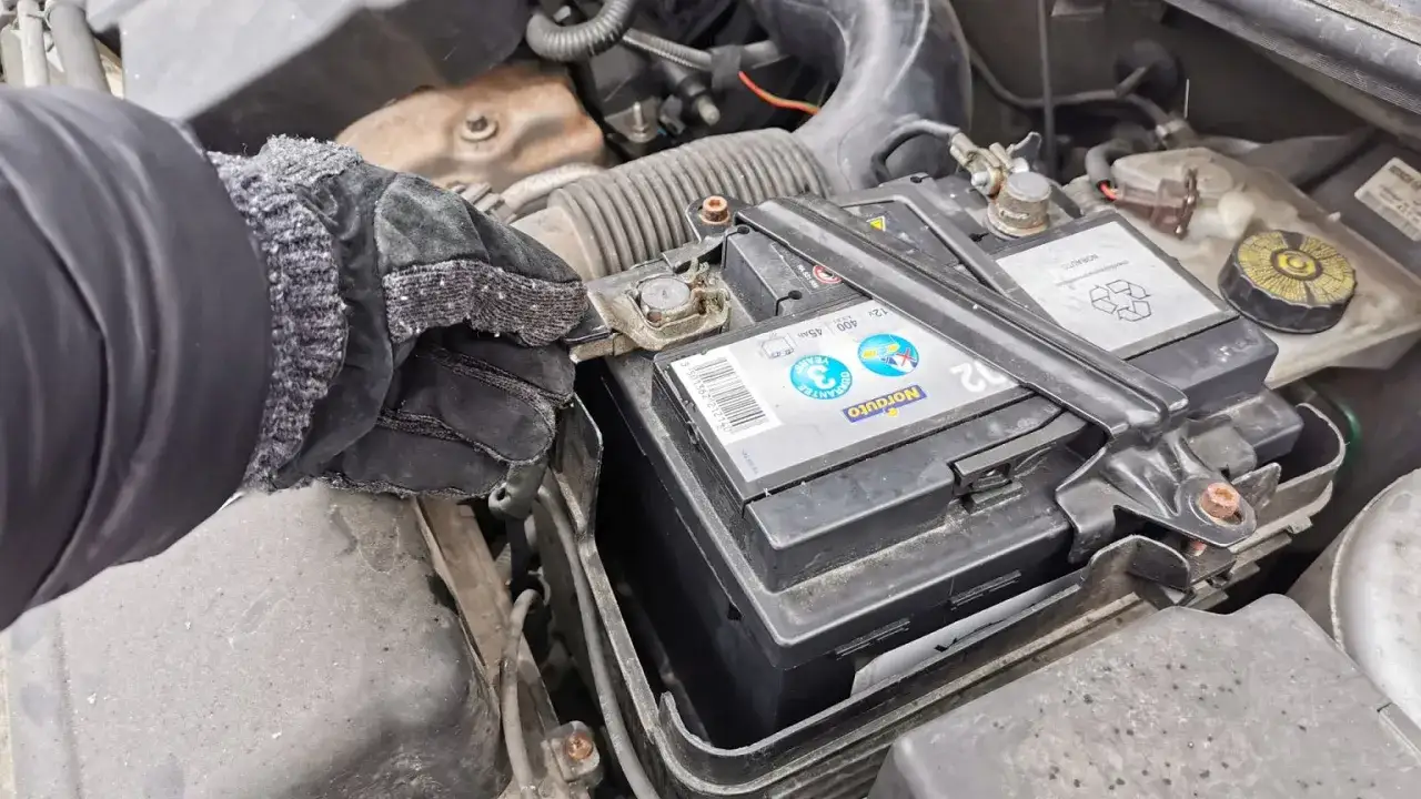 Rękawica w ręku pokazuje, jak założyć klemy na akumulator. Widać zacisk na biegunie.