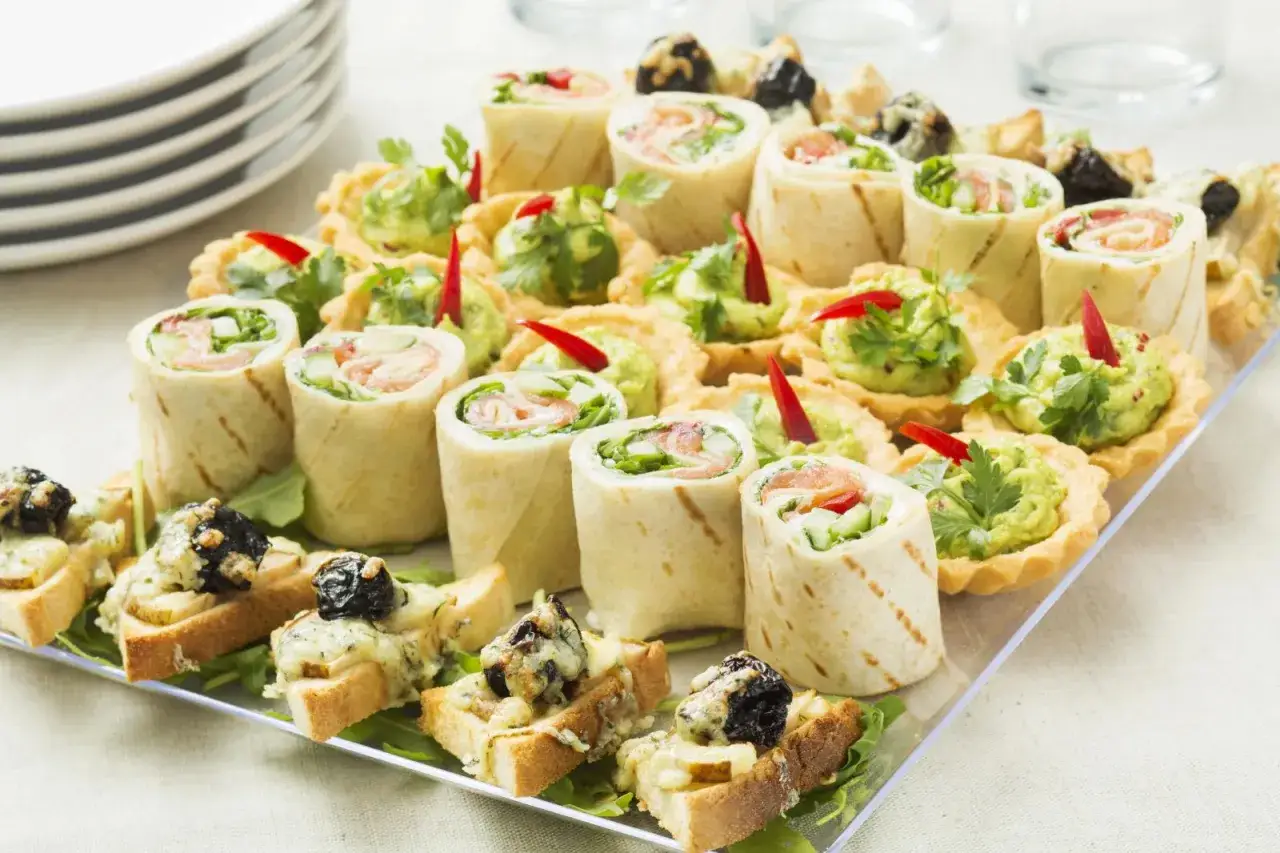 Talerz przekąsek: roladki z łososiem, tartaletki z guacamole i grzanki z serem. Idealne na imprezę, zastanawiasz się, ile kosztuje catering na 18?