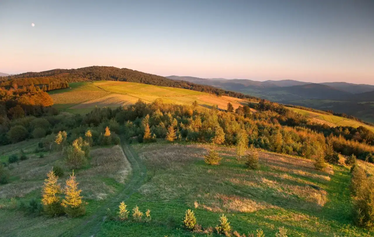 Zach&oacute;d słońca nad Beskidem Niskim, gdzie najpiękniejsze szlaki prowadzą przez złote pola i lasy. Księżyc w pełni obserwuje ten malowniczy krajobraz.