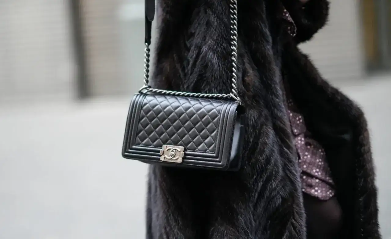 Elegancka, pikowana torebka Chanel czarna z łańcuszkiem, noszona na futrzanym płaszczu.
