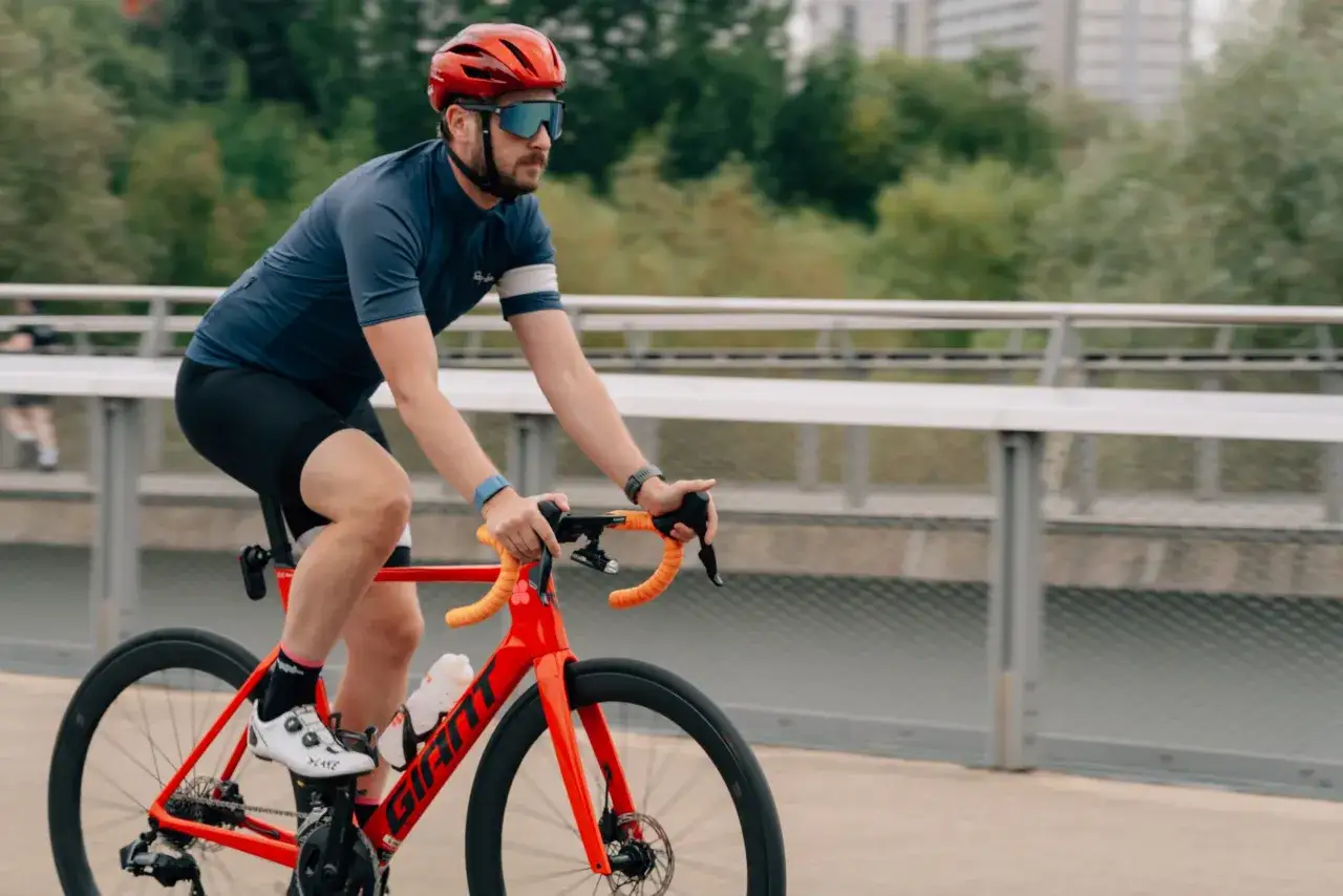 Mężczyzna w kasku i okularach jedzie na czerwonym rowerze. To świetny przykład, jak dopasować rower do swoich potrzeb, by jazda była komfortowa i bezpieczna.