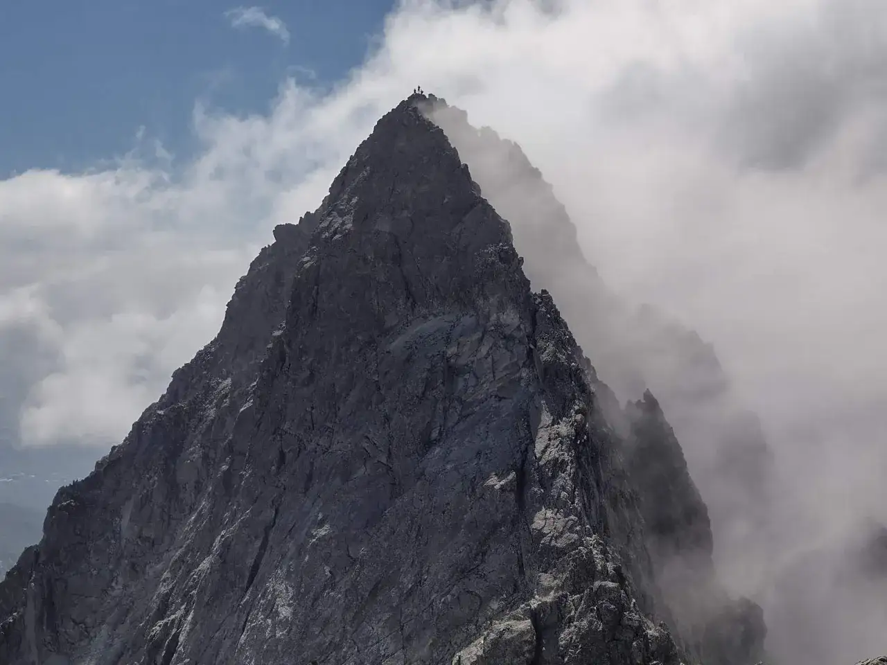 Szczyt górski otoczony chmurami. Na wierzchołku widać kilka postaci, które pokonały trudną drogę Martina.