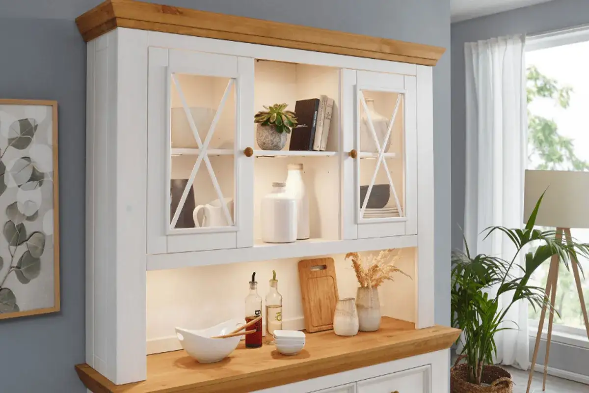 Biały kredens z drewnianym blatem i ozdobnymi szybkami. Jak wkomponować stary kredens w nowoczesne wnętrze? Oto inspiracja: biały mebel z przeszklonymi drzwiczkami, pełen dekoracji.