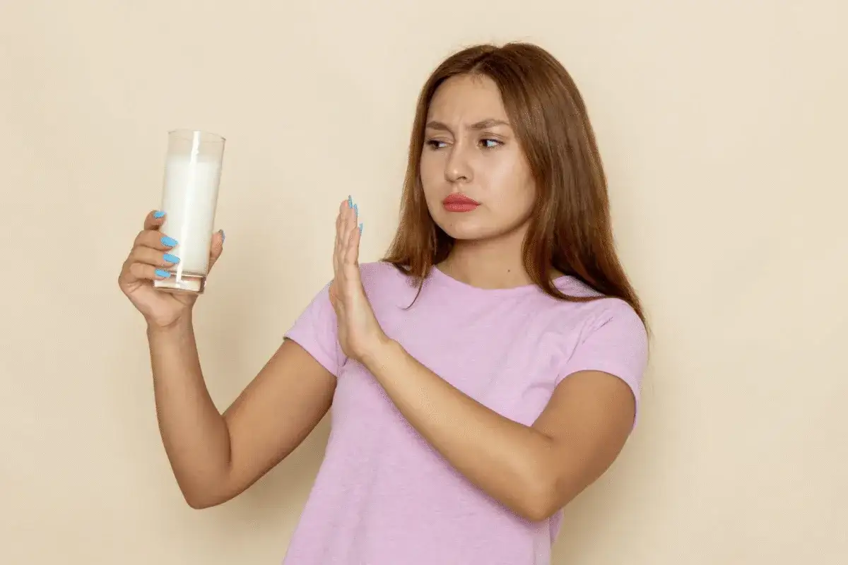 Młoda kobieta z niechęcią odrzuca szklankę mleka, sugerując, czy laktoza jest potrzebna jej organizmowi.