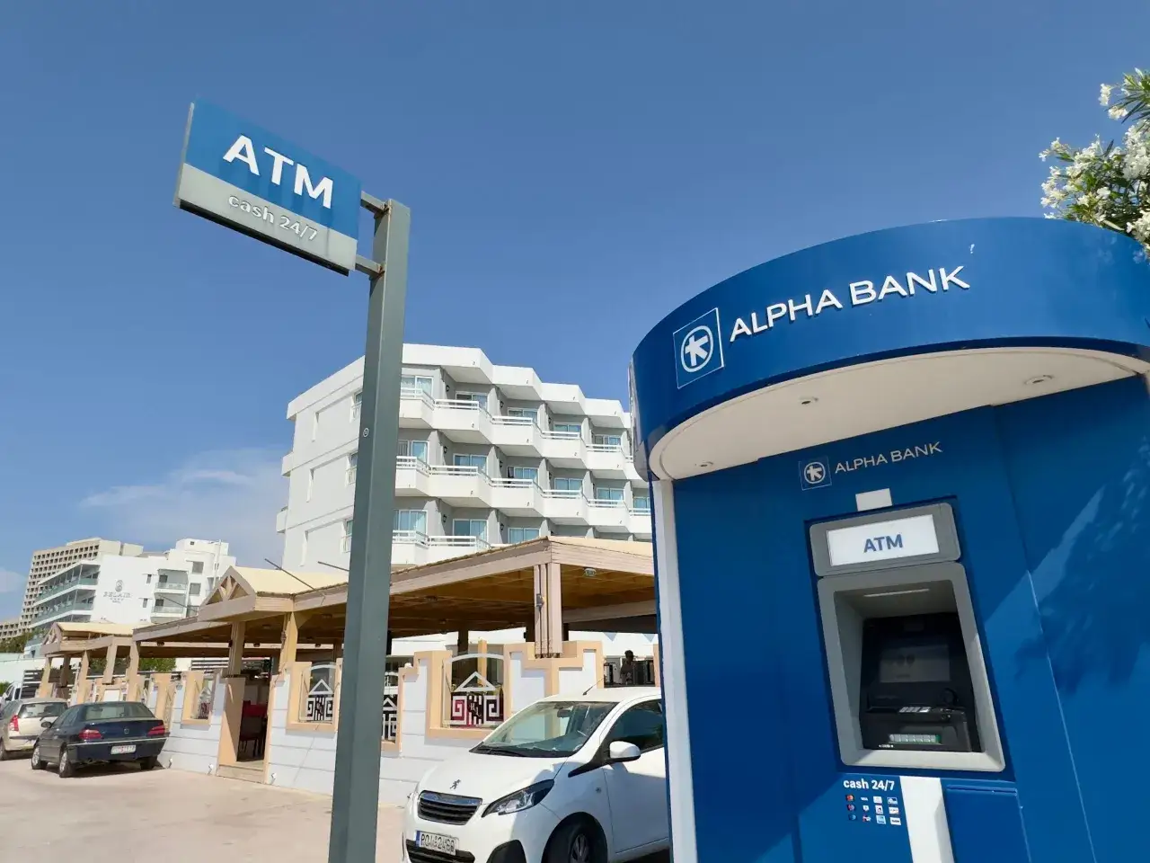 Bankomat Alpha Bank w Grecji, gdzie można wypłacić euro. W tle hotel i restauracja.