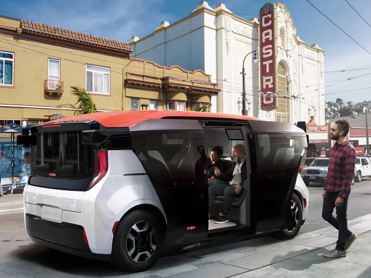 Autonomiczne pojazdy Cruise jadą ulicą San Francisco. W środku siedzą pasażerowie, a obok idzie mężczyzna.