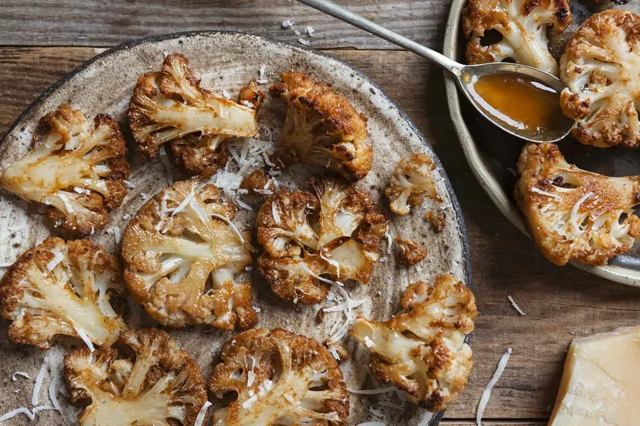 Pieczony kalafior z parmezanem, idealny pomysł co do kalafiora na obiad. Złociste różyczki na talerzu, posypane startym serem.