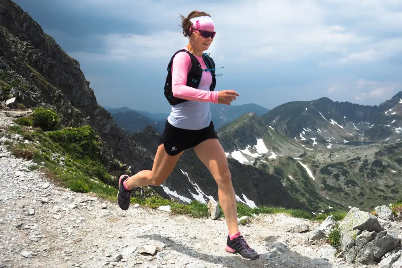 Kobieta w sportowym stroju biegnie po górskim szlaku, ciesząc się bieganiem po górach.