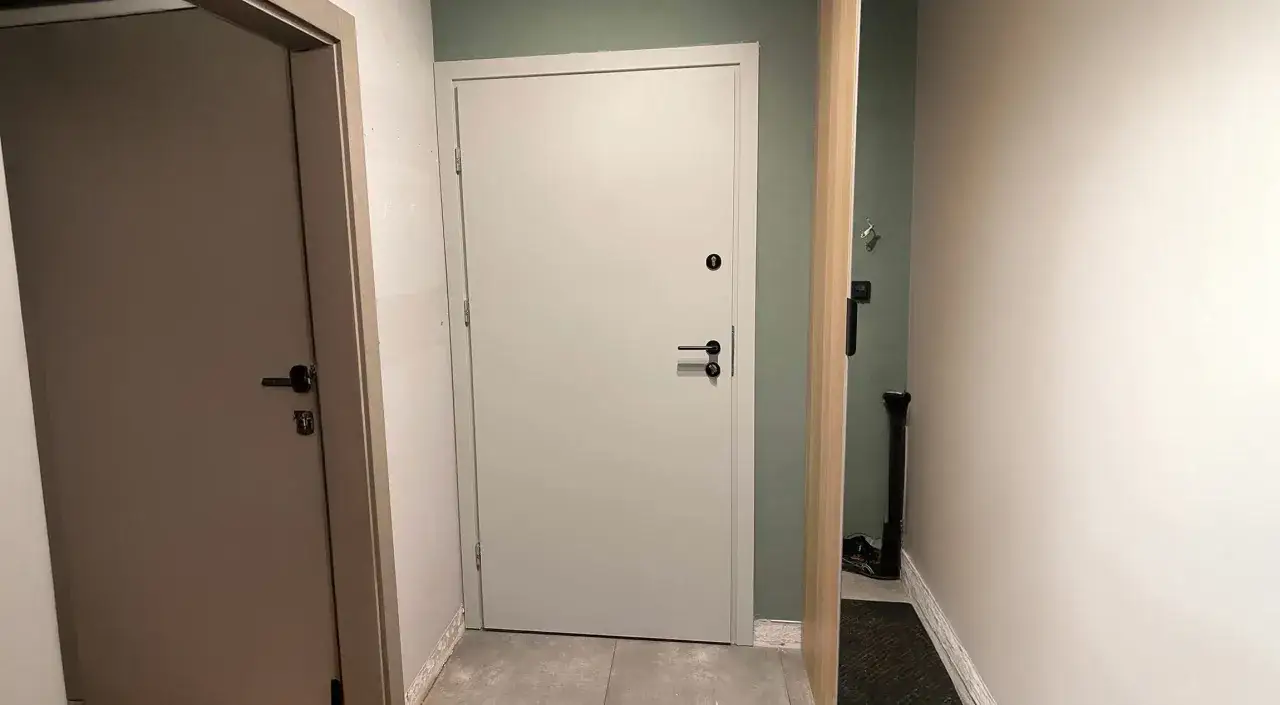 Przedstawiamy jak okleić drzwi okleiną samoprzylepną. Dwoje drzwi w korytarzu, jedno jasnoszare, drugie białe.