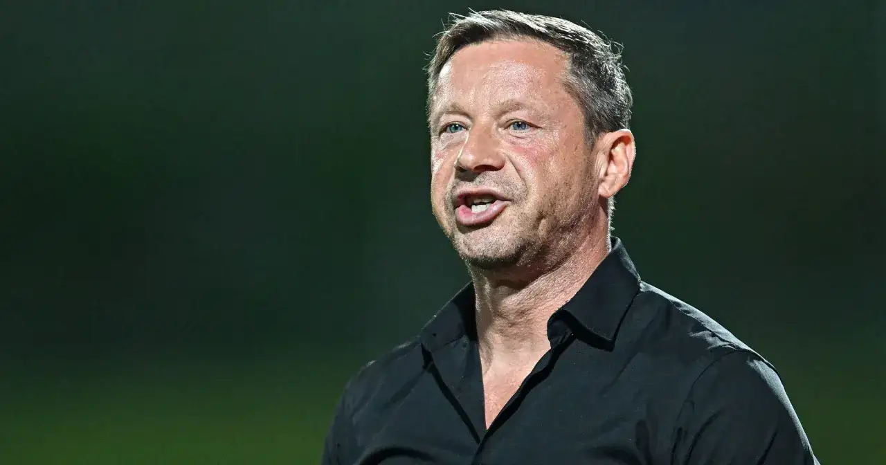 Trener Arki Gdynia w czarnej koszuli, dyskutujący o pogłoskach transferowych.