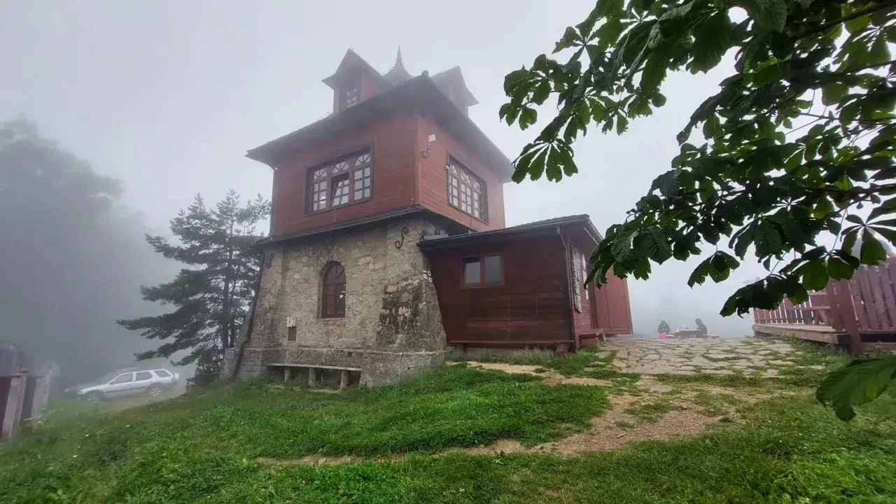 Drewniany budynek schroniska na Luboniu Wielkim we mgle. Obok stoi srebrny samochód.