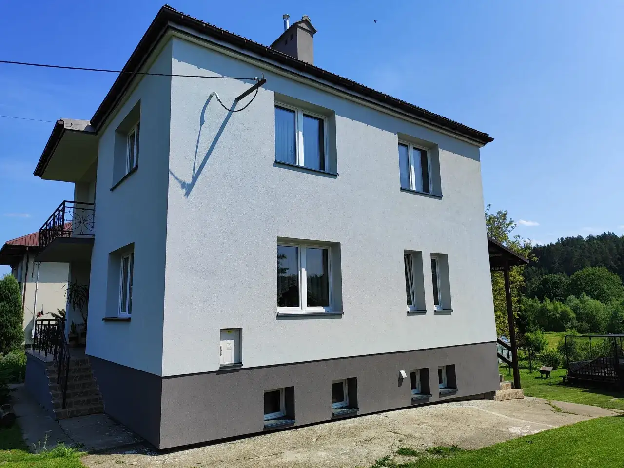 Dom z jasnoszarą elewacją i ciemnoszarą podstawą. Widać okna, balkon i komin. Zastanawiasz się, ile pelletu potrzeba na zimę?