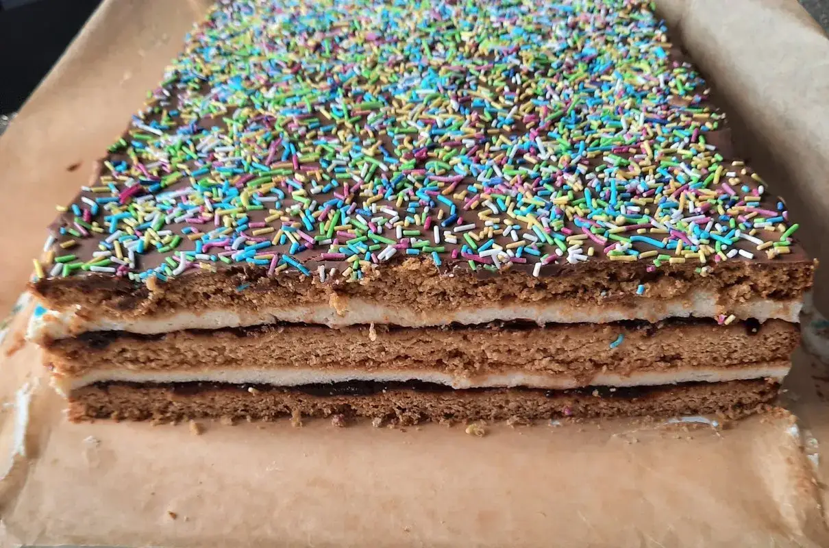 Pyszny miodownik z kaszą manną, przełożony kremem i dżemem, polany czekoladą i posypany kolorową posypką. Idealny przepis na deser!