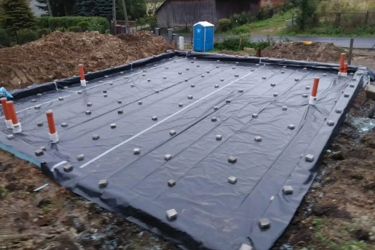 Fundament budowlany z folią i rurkami, na którym widać liczne dystanse do zbrojenia.