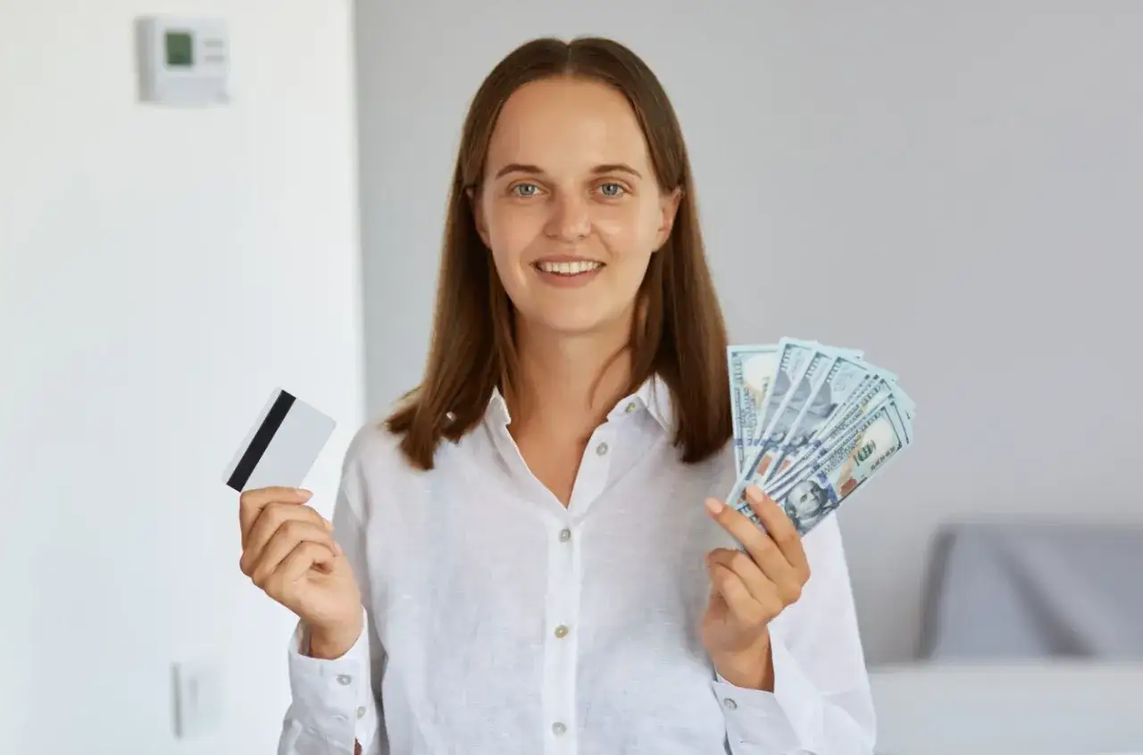 Uśmiechnięta kobieta trzyma kartę i banknoty. Zastanawia się, ile pozyczek mozna miec w Wonga, by sfinansować swoje marzenia.