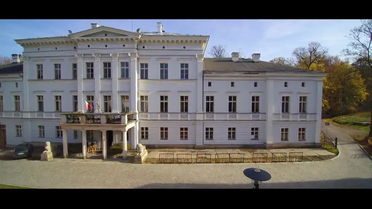 Elegancki pałac Jedlinka z białymi kolumnami i balkonem, otoczony jesiennym parkiem.