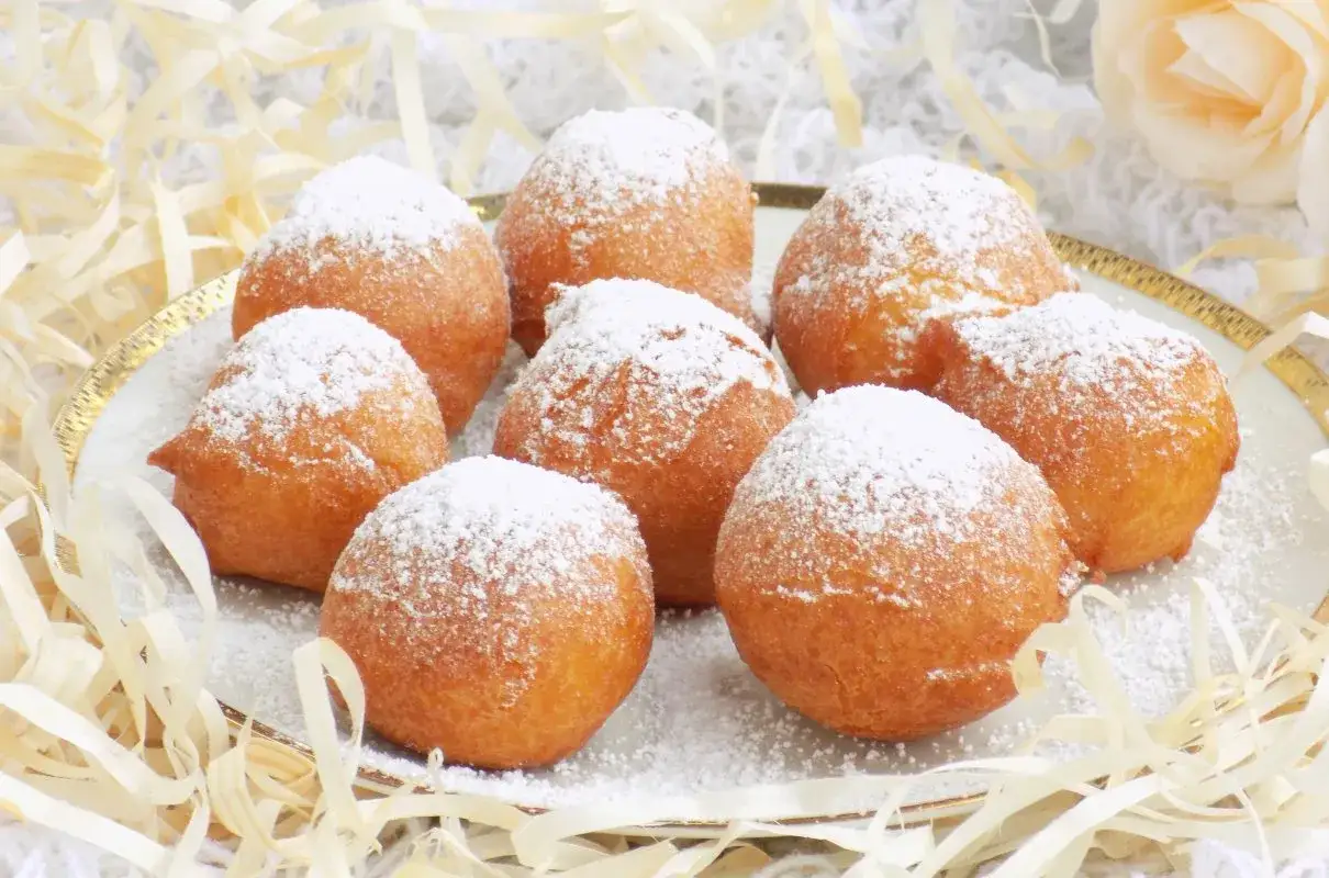 Puszyste pączki z serków homo, oprószone cukrem pudrem, wyglądają apetycznie na talerzu.