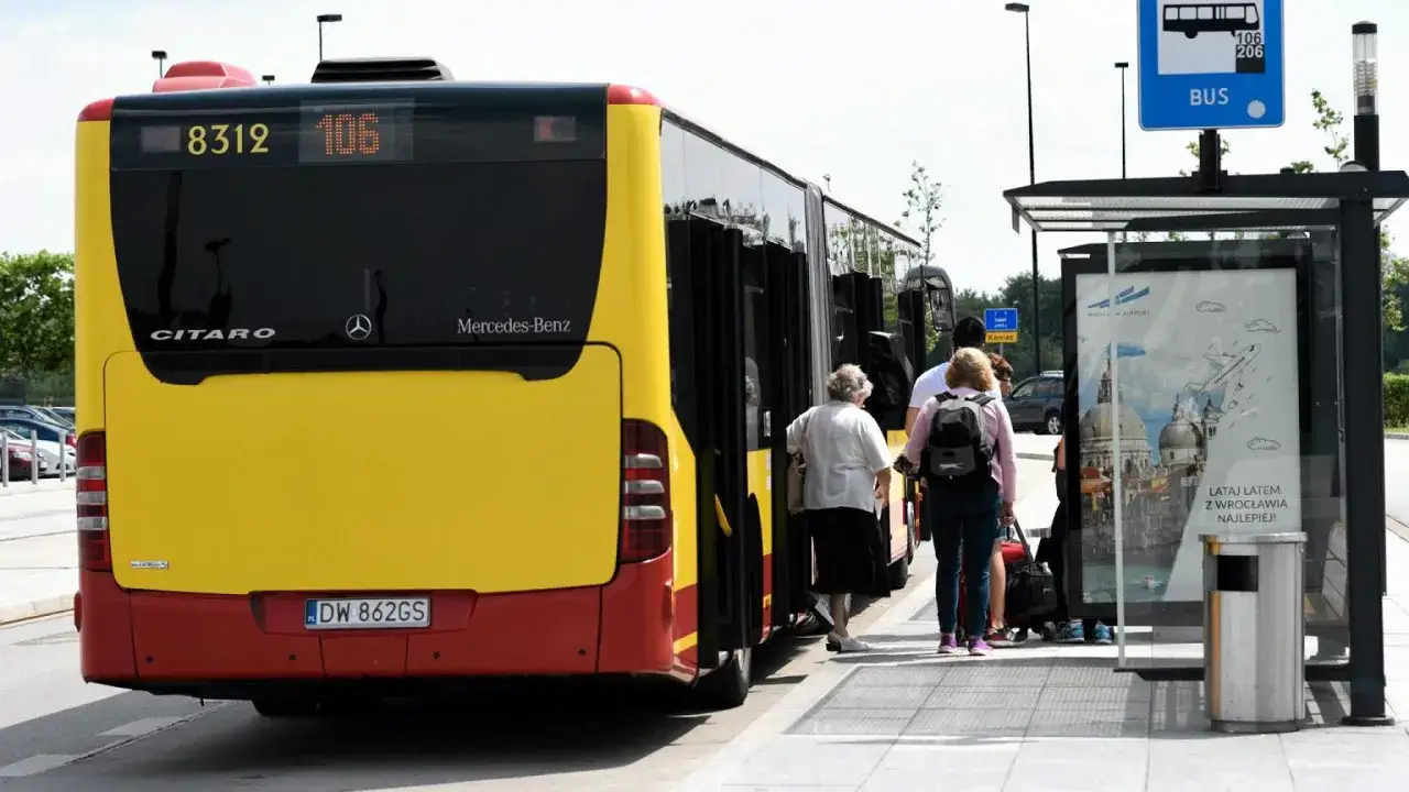 Żółty autobus wyjeżdżający z zatoki, czy ma pierwszeństwo? Ludzie wsiadają, czekając na przystanku.