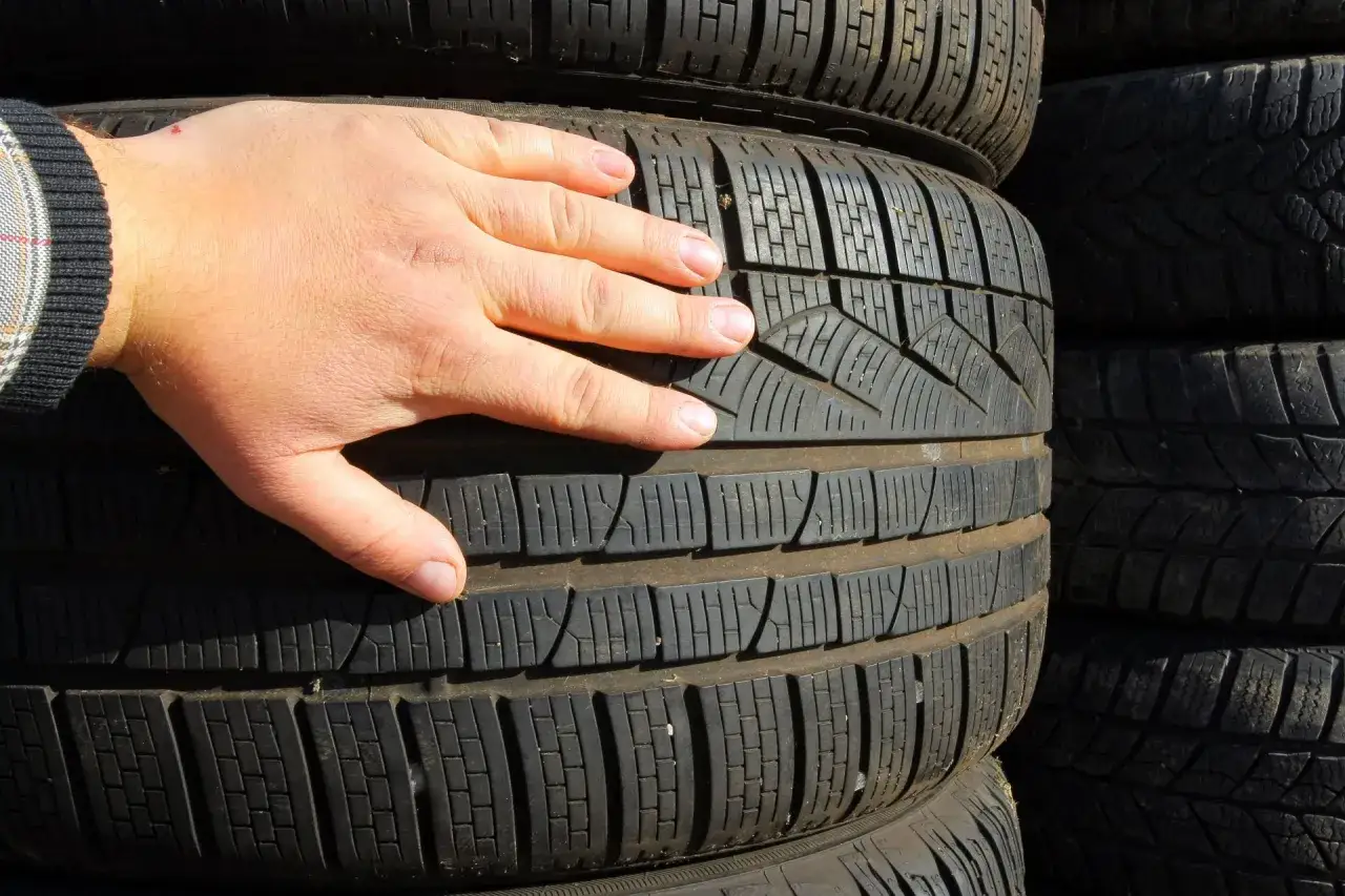 Dłoń sprawdza bieżnik nowej opony zimowej, szacując, ile mm bieżnika ma nowa opona zimowa.