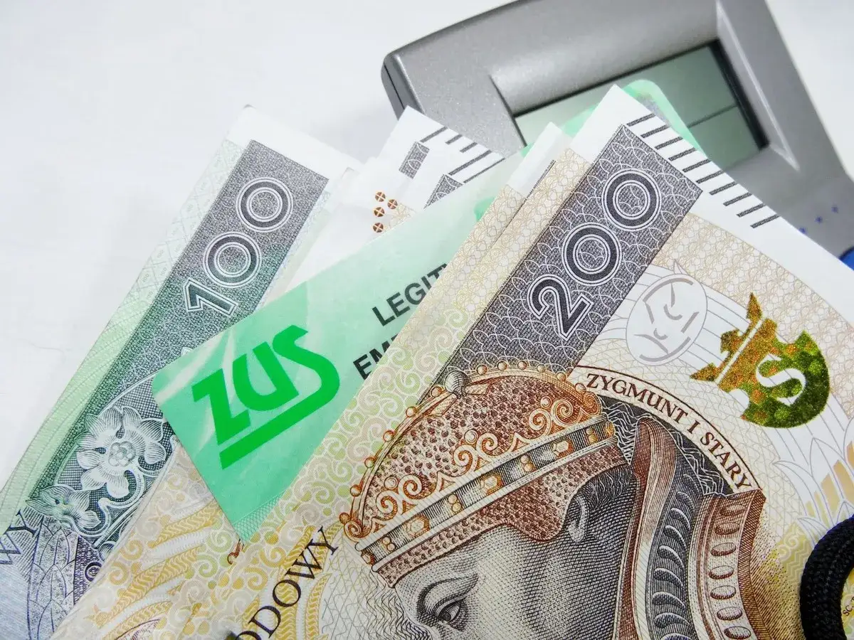 Złotówki i zielona karta ZUS leżą obok kalkulatora. Czy emeryta obowiązuje okres wypowiedzenia?