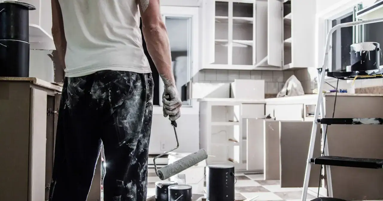 Malowanie kuchni, przygotowania do remontu. Jak zlikwidować łuki w domu? Malarz z wałkiem w ręku, puszki z farbą i drabina.