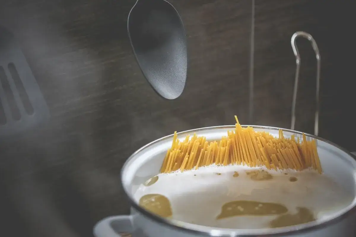 Gotujesz spaghetti, które może się skleić, jeśli nie będziesz uważać. Czarny łopatka wisi nad garnkiem.