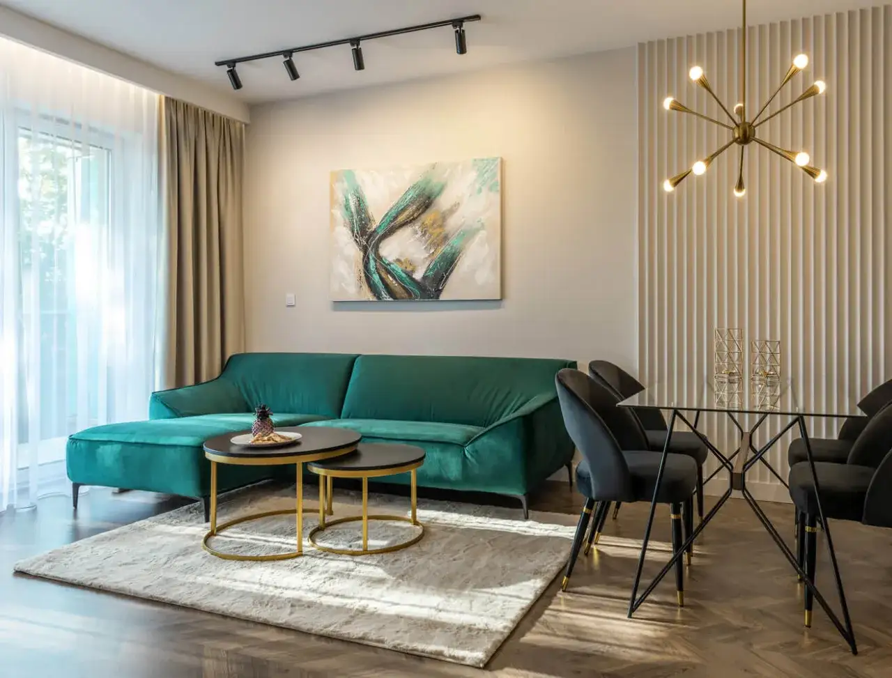 Elegancki salon z butelkowozieloną kanapą. Złote dodatki i czarne krzesła tworzą stylowe połączenie, pokazując, jaki kolor pasuje do butelkowej zieleni.