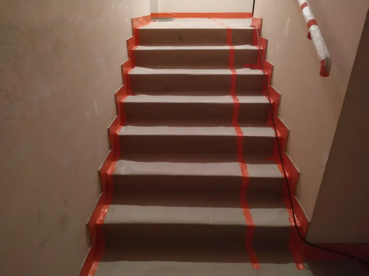 Schody zabezpieczone folią i taśmą malarską. To prosty sposób, jak zabezpieczyć schody przed malowaniem, chroniąc je przed zabrudzeniem.