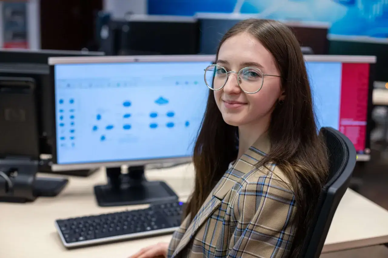 Młoda kobieta w okularach siedzi przy komputerze, pracując nad projektem. Zastanawia się, ile zarabia montażysta filmów.