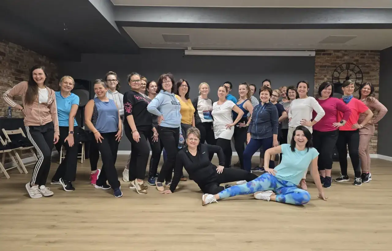 Grupa kobiet w sportowych strojach, uśmiechnięta, pozuje po udanym kursie tańca.