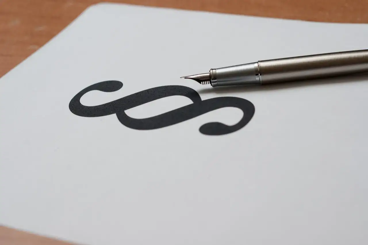 Elegancki długopis spoczywa obok symbolu paragrafu na białej kartce.