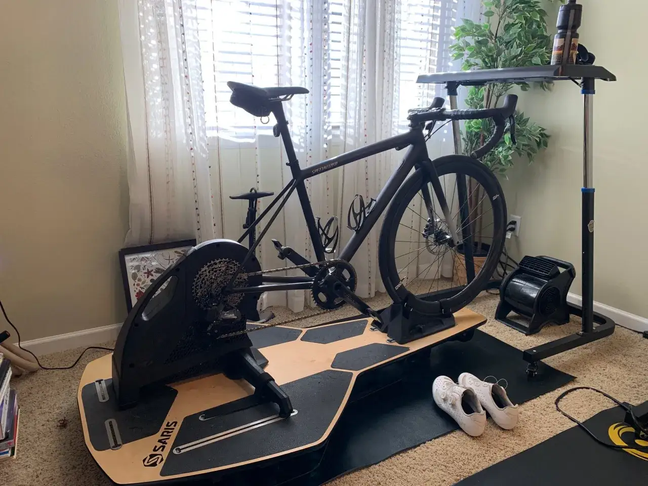 Gotowy do treningu na trenażerze? Rower Specialized czeka na platformie Saris, obok wentylatora i but&oacute;w kolarskich.